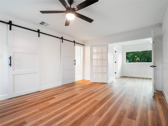 interior space with a barn door, ceiling fan, and light hardwood / wood-style flooring