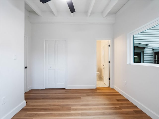 unfurnished bedroom featuring hardwood / wood-style floors, beam ceiling, a closet, and ensuite bath