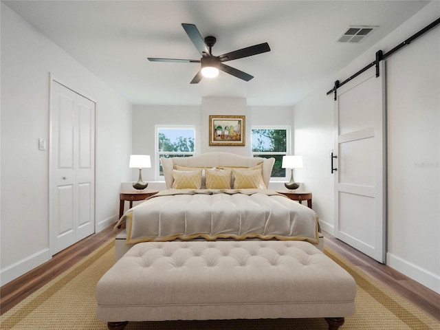 bedroom with ceiling fan, a barn door, light hardwood / wood-style floors, and a closet