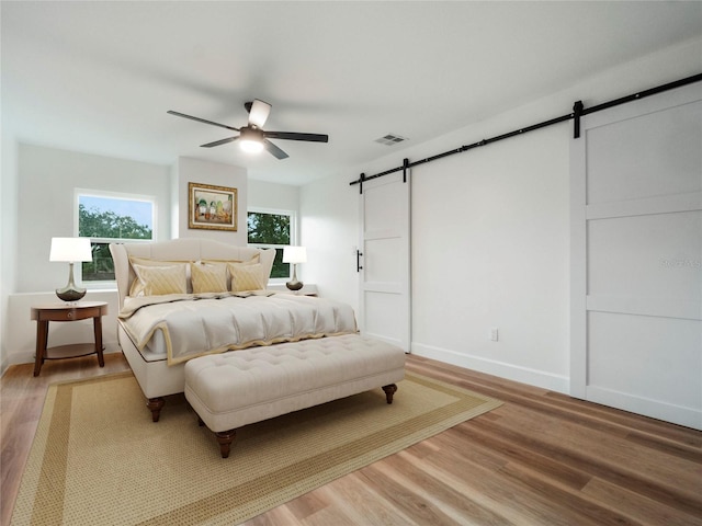 bedroom with hardwood / wood-style floors, ceiling fan, and a barn door