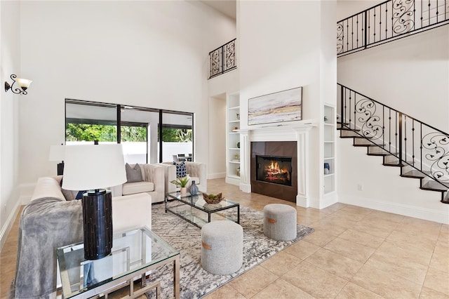 living room with light tile patterned flooring, built in shelves, a high ceiling, and a tiled fireplace