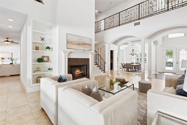 tiled living room featuring ceiling fan with notable chandelier, built in features, a towering ceiling, and ornate columns