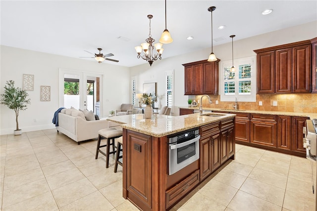 kitchen featuring french doors, a kitchen island with sink, sink, pendant lighting, and oven