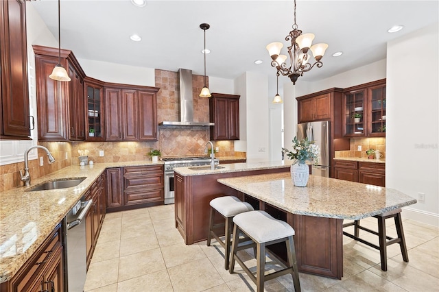 kitchen with pendant lighting, a kitchen island with sink, wall chimney range hood, sink, and appliances with stainless steel finishes