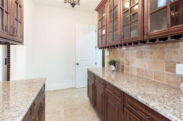 kitchen featuring dark brown cabinets, light stone counters, light tile patterned floors, and tasteful backsplash