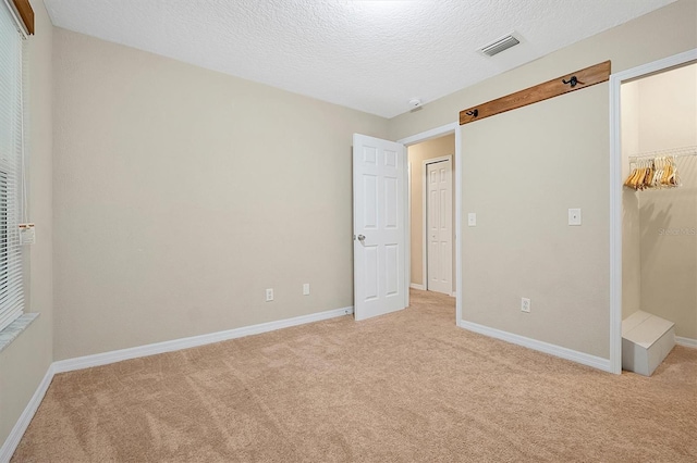 unfurnished bedroom with a walk in closet, light carpet, a closet, and a textured ceiling