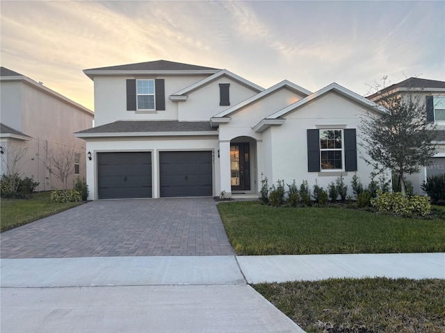 traditional home featuring a garage, a yard, decorative driveway, and stucco siding