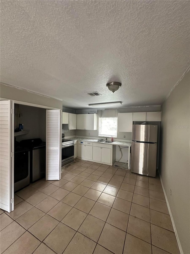 kitchen with sink, a textured ceiling, light tile patterned flooring, white cabinetry, and stainless steel appliances