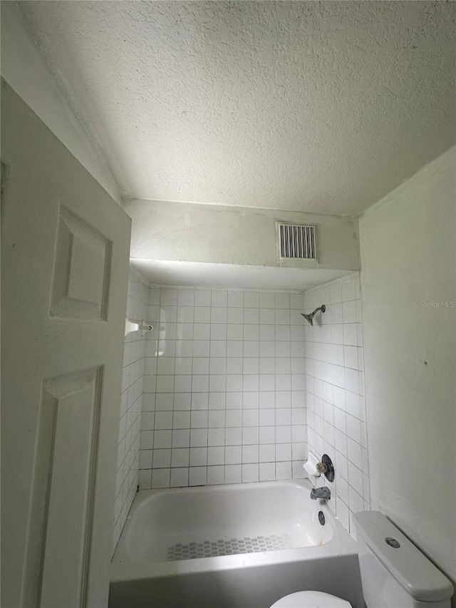 bathroom featuring a textured ceiling, toilet, and tiled shower / bath