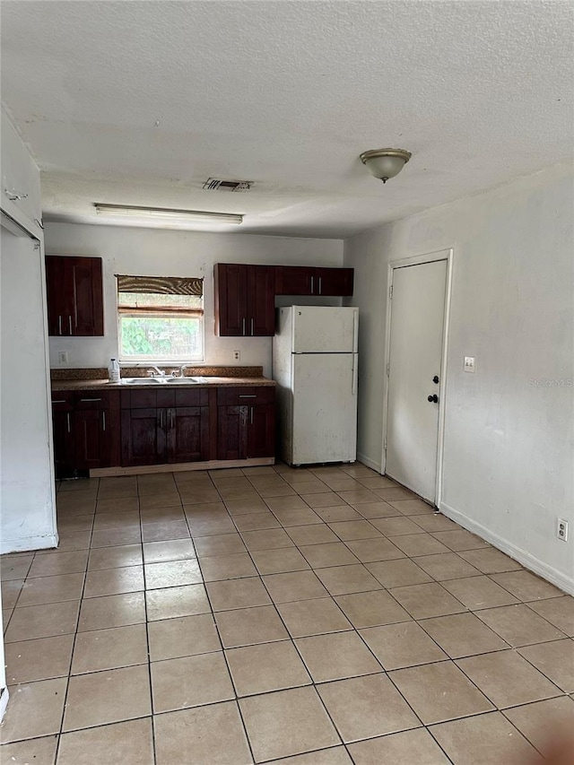 kitchen featuring dark brown cabinetry, sink, light tile patterned flooring, and white refrigerator