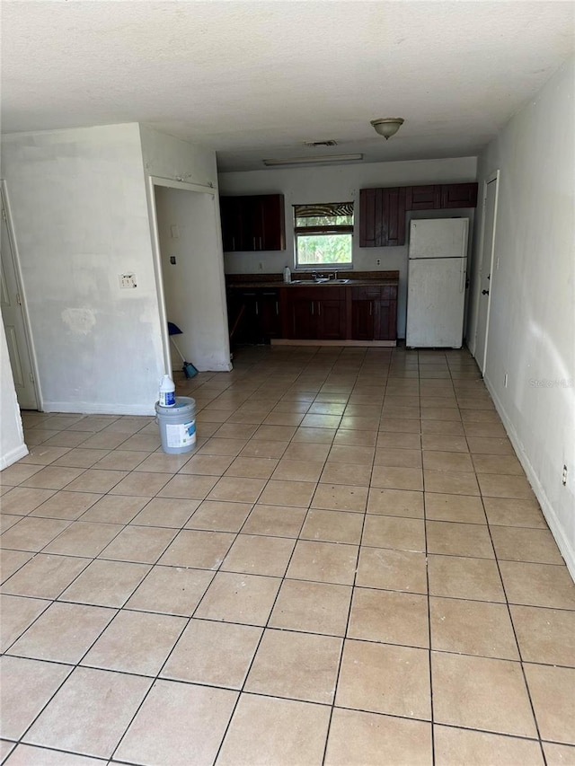 kitchen featuring dark brown cabinets, white fridge, light tile patterned floors, and sink