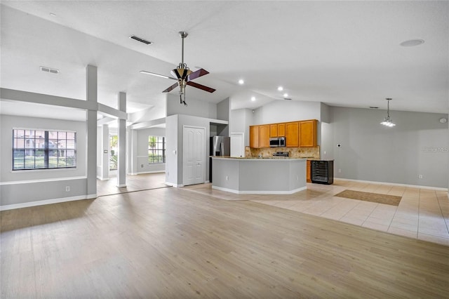 unfurnished living room featuring light wood-type flooring, vaulted ceiling, ceiling fan, and ornate columns