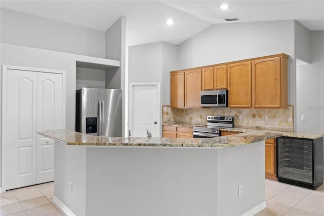 kitchen featuring appliances with stainless steel finishes, light tile patterned floors, a center island, and vaulted ceiling