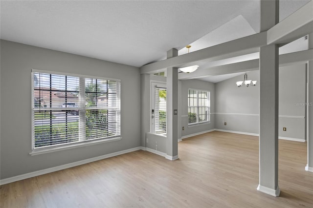 unfurnished room featuring hardwood / wood-style flooring, lofted ceiling, a textured ceiling, and an inviting chandelier