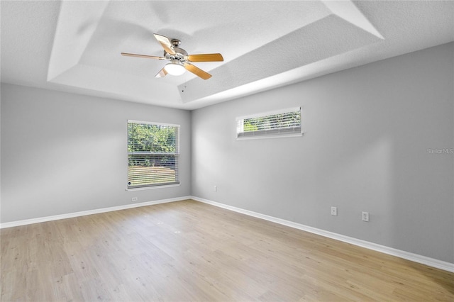 unfurnished room with ceiling fan, a raised ceiling, light wood-type flooring, and a textured ceiling