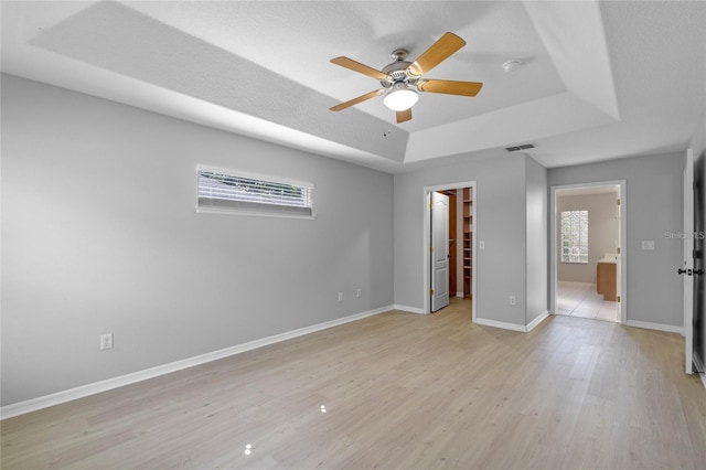 unfurnished bedroom featuring a raised ceiling, ensuite bath, ceiling fan, a spacious closet, and a closet