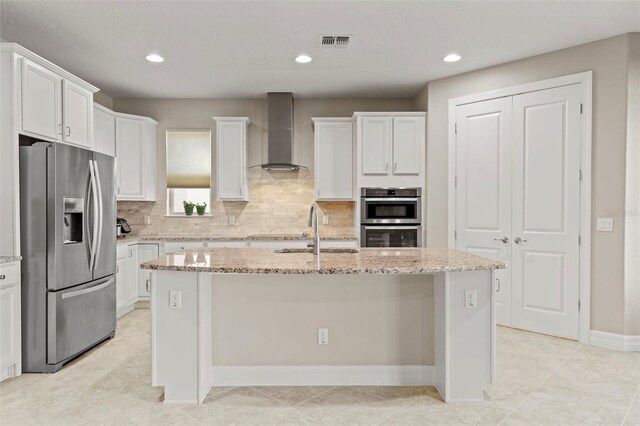 kitchen featuring sink, an island with sink, stainless steel appliances, and wall chimney range hood