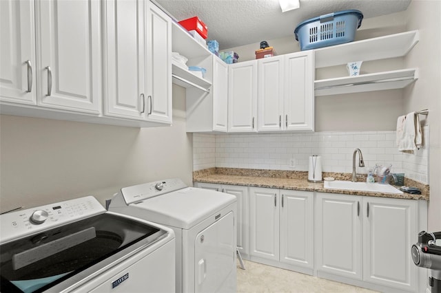 laundry room with cabinets, a textured ceiling, separate washer and dryer, and sink