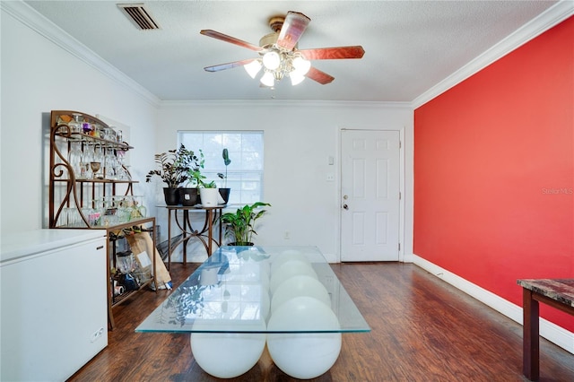 dining area featuring a textured ceiling, dark wood-type flooring, crown molding, and ceiling fan