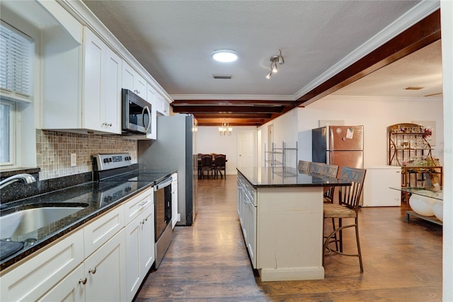 kitchen featuring white cabinets, a kitchen bar, stainless steel appliances, dark stone counters, and beam ceiling