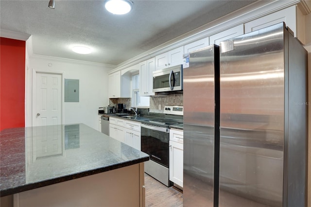 kitchen with appliances with stainless steel finishes, white cabinetry, dark stone counters, ornamental molding, and electric panel
