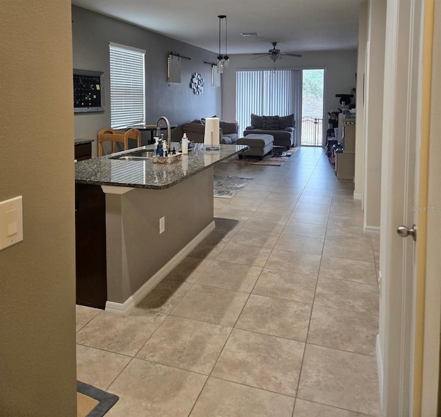 kitchen with pendant lighting, dark stone countertops, ceiling fan, a kitchen breakfast bar, and sink