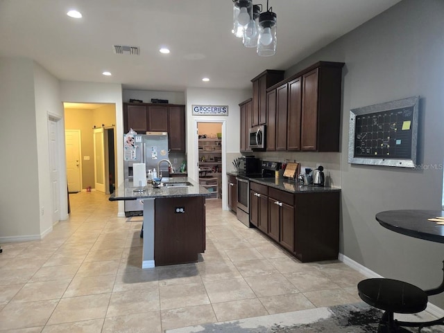 kitchen featuring appliances with stainless steel finishes, an island with sink, dark stone counters, dark brown cabinetry, and sink