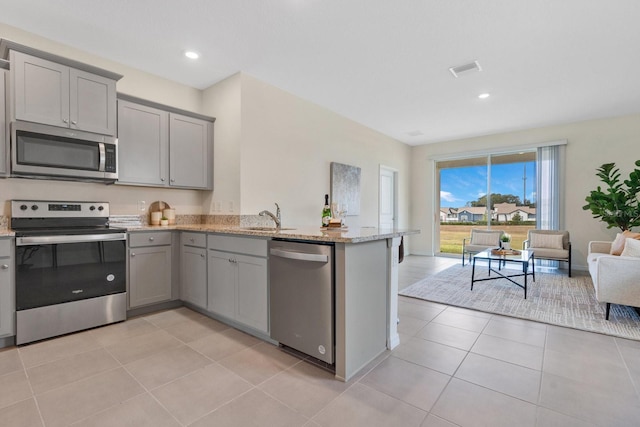 kitchen with light stone countertops, appliances with stainless steel finishes, gray cabinets, and light tile patterned floors