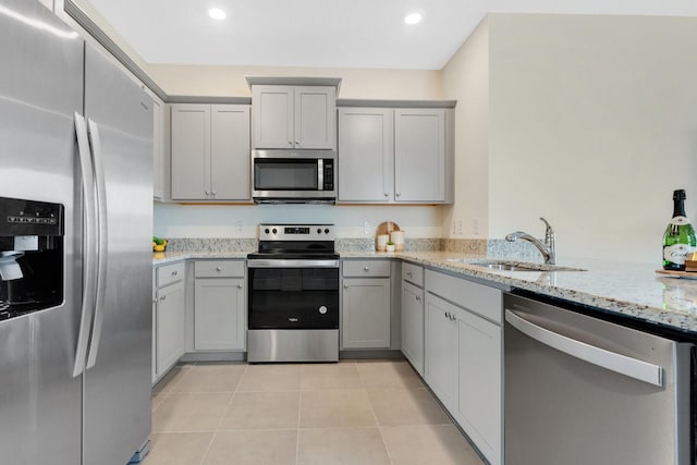 kitchen with gray cabinetry, light stone counters, sink, and appliances with stainless steel finishes