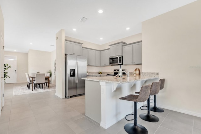 kitchen with kitchen peninsula, stainless steel appliances, light tile patterned floors, gray cabinets, and a breakfast bar area