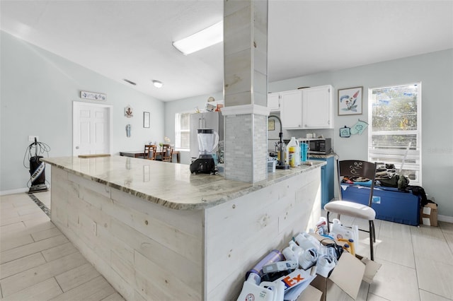 kitchen with lofted ceiling, light stone counters, white cabinetry, and light tile patterned floors