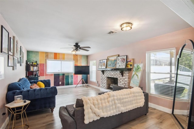 living room featuring a wealth of natural light, light hardwood / wood-style flooring, ceiling fan, and a brick fireplace