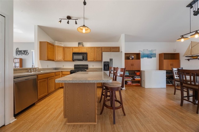 kitchen featuring light wood-type flooring, sink, black appliances, pendant lighting, and a kitchen island