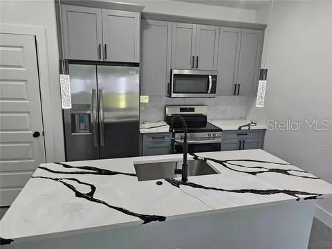 kitchen featuring backsplash, light stone countertops, stainless steel appliances, gray cabinetry, and a sink