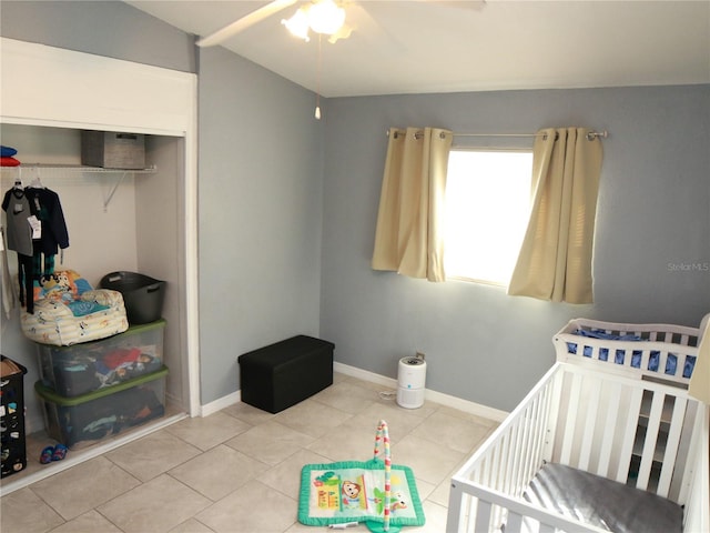 bedroom with a crib, tile patterned flooring, a closet, and ceiling fan