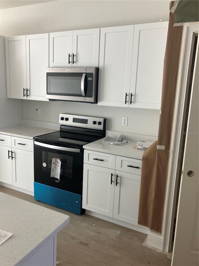 kitchen with electric range, light wood-style flooring, stainless steel microwave, light stone countertops, and white cabinetry