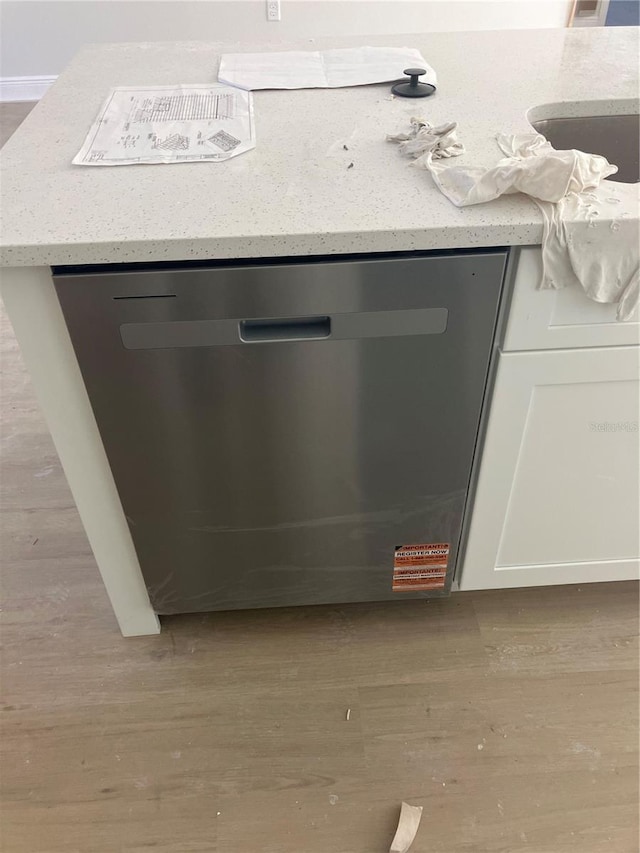 interior details featuring white cabinetry, a sink, stainless steel dishwasher, and wood finished floors