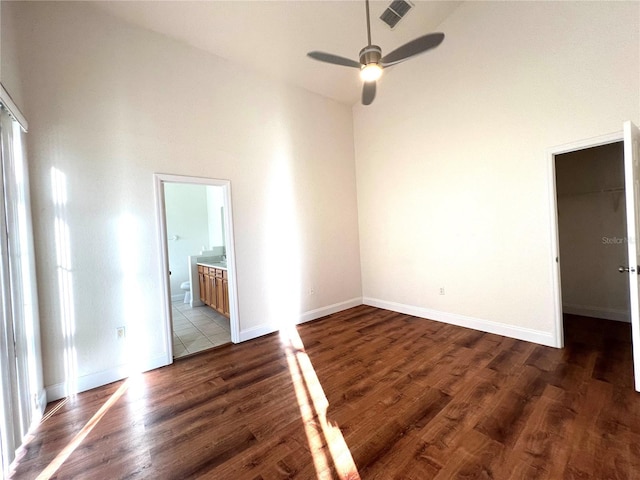 empty room featuring ceiling fan, a towering ceiling, and dark wood-type flooring