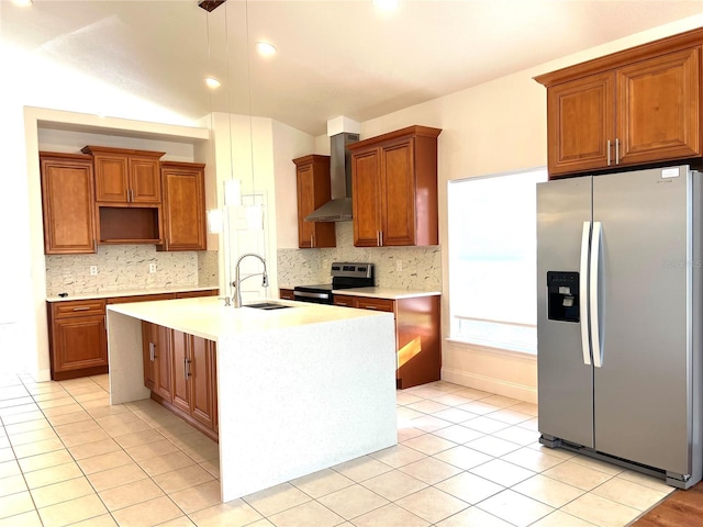 kitchen with appliances with stainless steel finishes, sink, wall chimney range hood, decorative light fixtures, and an island with sink