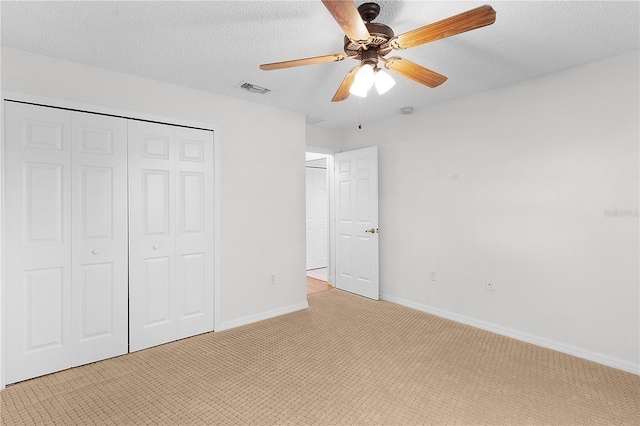 unfurnished bedroom with ceiling fan, a closet, light colored carpet, and a textured ceiling