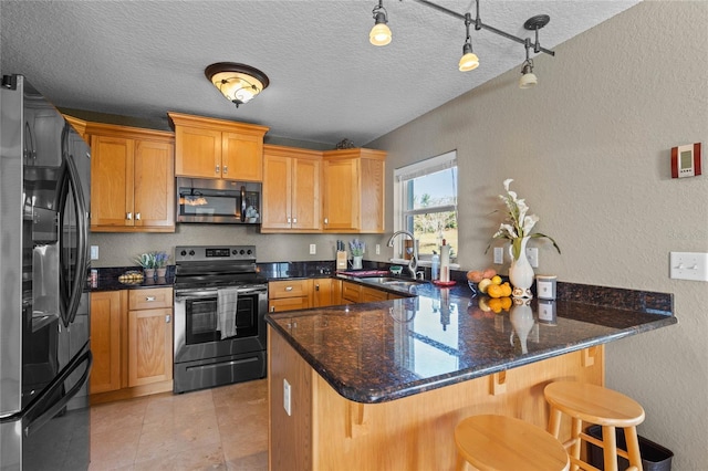 kitchen with sink, stainless steel appliances, dark stone countertops, a textured ceiling, and a breakfast bar area