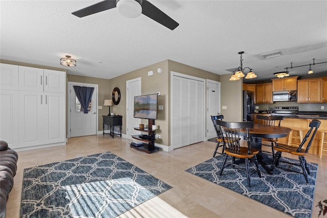 dining room featuring a textured ceiling, track lighting, and ceiling fan with notable chandelier