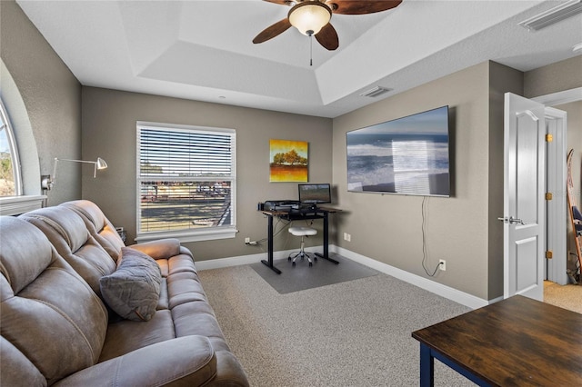 carpeted living room with a raised ceiling and ceiling fan