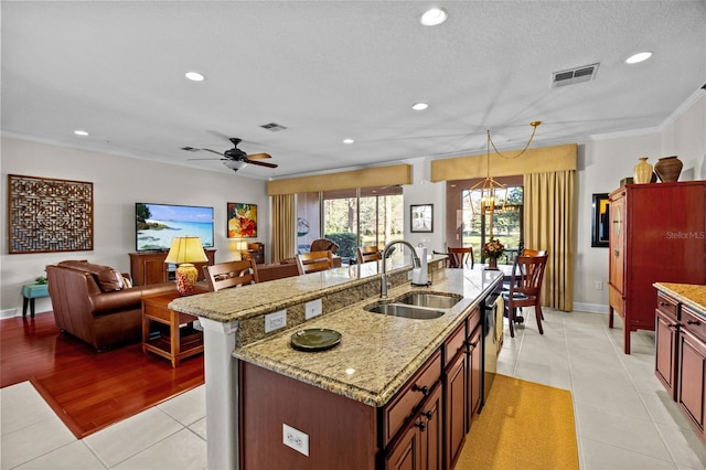 kitchen with crown molding, light tile patterned floors, sink, ceiling fan with notable chandelier, and a center island with sink