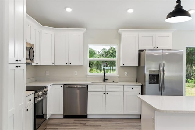 kitchen featuring white cabinetry, sink, stainless steel appliances, and decorative light fixtures