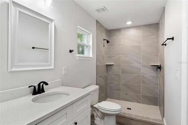 bathroom featuring a tile shower, vanity, and toilet