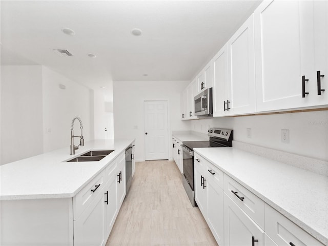 kitchen with sink, light hardwood / wood-style flooring, a center island with sink, white cabinets, and appliances with stainless steel finishes