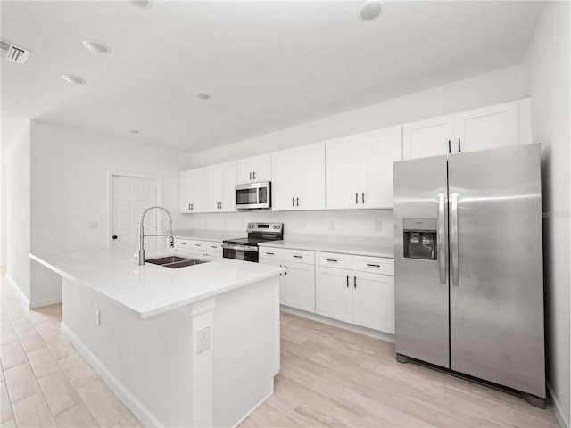 kitchen featuring light wood-type flooring, stainless steel appliances, sink, white cabinetry, and an island with sink