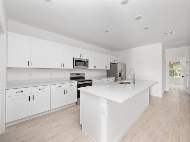 kitchen featuring white cabinetry, sink, stainless steel appliances, a center island with sink, and light wood-type flooring