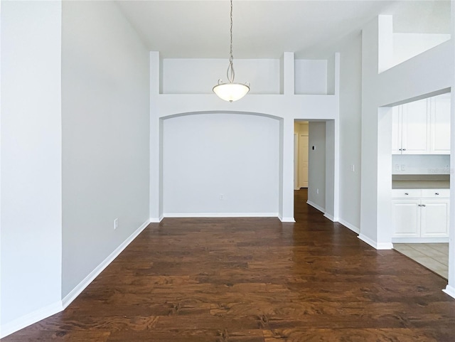 unfurnished dining area featuring a towering ceiling and dark hardwood / wood-style flooring